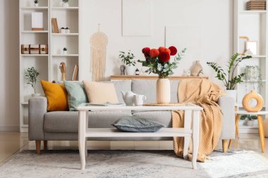 Konforlu kanepe ve vazodaki yıldız çiçekleri oturma odasındaki cam sehpanın üzerinde.