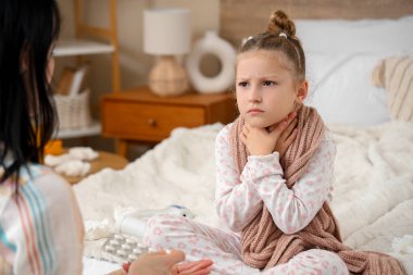 Boğazı ağrıyan hasta küçük bir kız ve annesi yatak odasında.