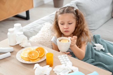 Boğazı ağrıyan hasta küçük kız evde raftan bir bardak limon çayı alıyor.