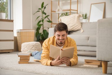 Genç adam evde halıda kitap okuyor.