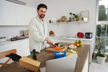 Bilgisayarlı yakışıklı sakallı adam mutfakta dolma biber kesiyor.