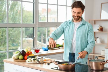 Yakışıklı sakallı adam mutfakta kızarmış sebzelerin üzerine yağ döküyor.