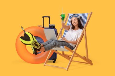 Kokteyl ve dizüstü bilgisayarlı genç iş kadını sarı arka planda yaz tatilini bekliyor.