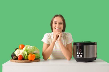 Sofrada yeşil arka planda çoklu fırın ve sebzeli genç bir kadın.