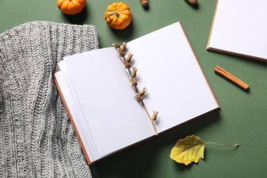 Boş bir kitap, yeşil arka planda örülmüş eşarp ve balkabakları.