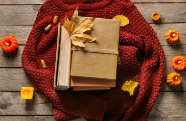 Kitap yığını, sıcak süveter, yanan mumlar ve ahşap arka planda sonbahar dekoru olan kompozisyon