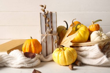 Kitaplı kompozisyon, farklı balkabakları ve açık ahşap masada sıcak giysiler.