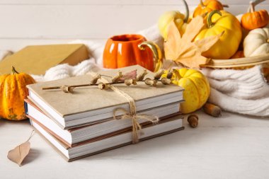 Kitap seti, balkabağı, sıcak kıyafetler ve açık ahşap masada bir fincan çay.