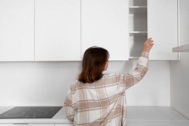 Mutfakta dolabı açan genç bir kadın.