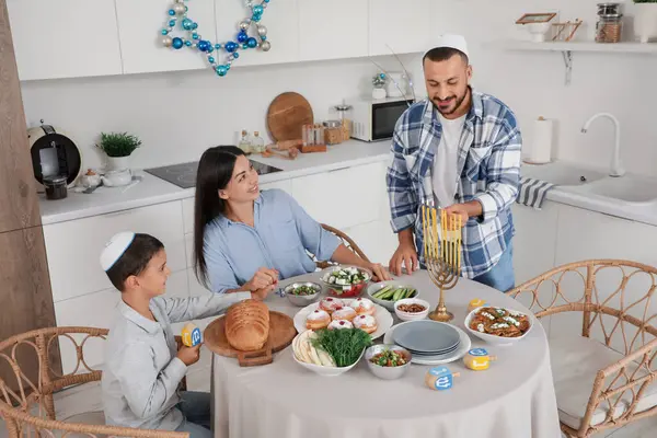 Mutlu aile, festival mutfağında servis edilen yemek masasında mum yakıyor. Hanuka kutlaması