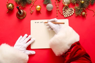 Noel Baba kırmızı arka planda Noel dekoru olan yapılacaklar listesi yazıyor