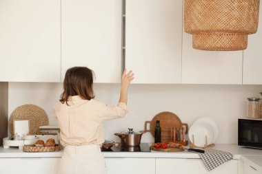 Mutfakta dolabı açan genç bir kadın.