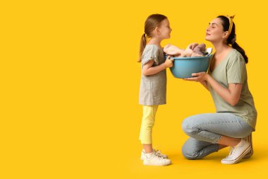 Sarı arka planda farklı temizlik malzemeleri olan mutlu anne ve kızı.