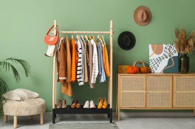 Asılı giysiler, çekmeceler ve soyunma odasındaki yeşil duvarın yanındaki yastıklı puf.