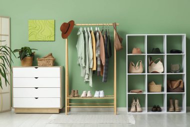 Askıda asılı şık sonbahar giysileri, çekmeceler ve yeşil duvara karşı raf ünitesi