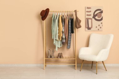 Soyunma odasındaki bej duvarın yanındaki koltuğu ve elbiseleri dizin.