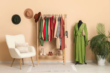 Giysilerle, koltukla ve mankenle birlikte soyunma odasındaki bej duvarın yanında.