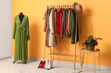 Soyunma odasındaki sarı duvarın yanında giysiler ve mankenlerle dizilin.