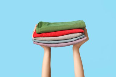 Mavi arka planda farklı giysi yığınları olan kadın elleri