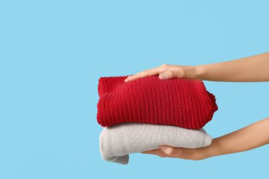 Mavi arka planda sıcak giysi yığını olan kadın elleri