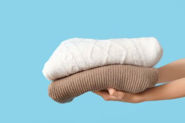 Mavi arka planda sıcak giysi yığını olan kadın elleri