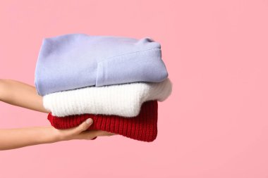 Pembe arka planda kalın giysileri olan kadın elleri.