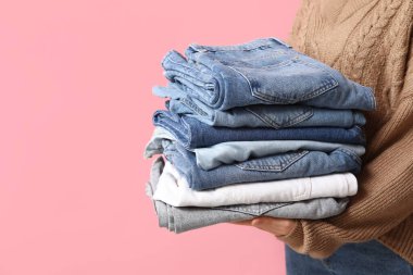 Pembe arka planda farklı kot pantolonları olan kadın, yakın plan.