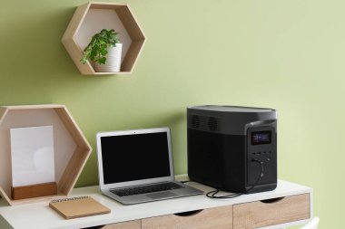 Ofisteki yeşil duvarın yanındaki masada dizüstü bilgisayarı olan taşınabilir elektrik santrali.