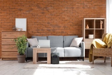 Oturma odasının içinde kanepe, dizüstü bilgisayar ve taşınabilir güç istasyonu var.