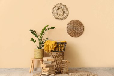 Bir yığın kitap, odada bej duvarın yanında ekoseli ve çiçekli sepet.