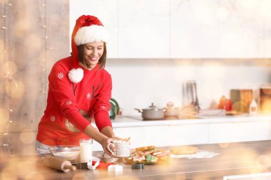 Noel arifesinde mutfaktaki masada elinde bir fincan kakao ve zencefilli kurabiye olan genç bir kadın.