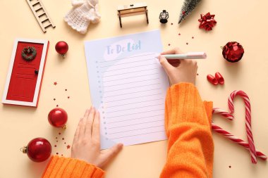 Bej arka planda Noel dekoru olan yapılacaklar listesi yazan kadın