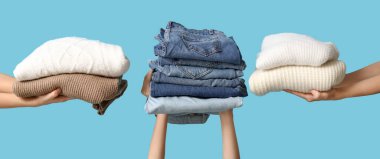 Dişi eller açık mavi arka planda bir yığın kıyafet tutuyor.  