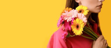 Sarı arka planda Gerbera çiçeği buketi tutan genç ve güzel bir kadın.