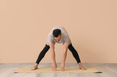 Yakışıklı adam bej duvarın yanında yoga yapıyor.