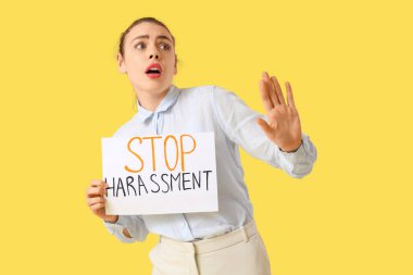 Elinde kağıt tutan genç iş kadını şok oldu. Sarı arka planda DUR HARASSMENT