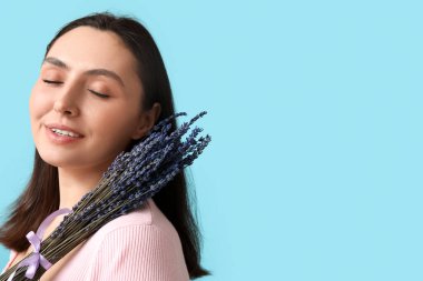 Mavi arka planda bir demet lavanta çiçeğiyle güzel genç bir kadın.