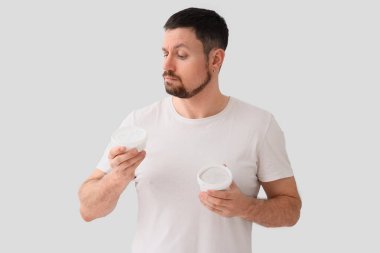 Hafif arka planda diş pudrası dolu kavanozları olan düşünceli genç bir adam.