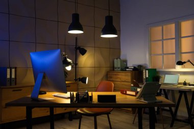 Masaları ve parlak lambaları olan karanlık ofisin içi.