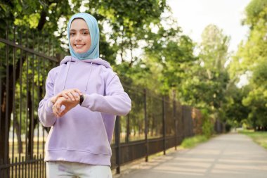 Parkta spor bileziği olan Müslüman bir kadın.