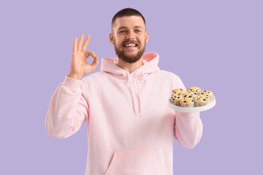 Lezzetli muffinleri olan genç adam leylak arka planda iyi görünüyor.