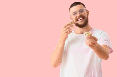 Pembe arka planda lezzetli muffinleri olan genç bir adam.