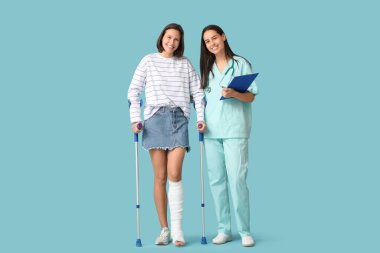 Young woman with broken leg and doctor on blue background clipart