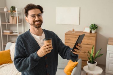 Evde e-okuyucusu ve kahve fincanı olan genç bir adam var.