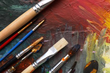 Ressam fırçaları ve bıçakları palette boyalarla, yakın plan.