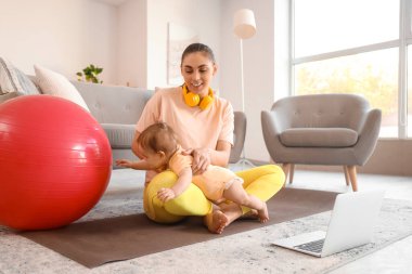 Küçük bebeğiyle evde yoga minderinde oturan sportif bir anne.