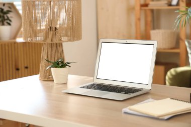 Oturma odasındaki programcının masasında bitki ve lamba olan boş bir dizüstü bilgisayar.