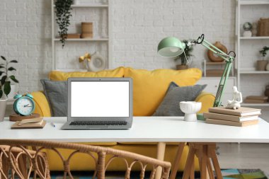 Oturma odasındaki programcının masasında lamba, kitap ve alarm saati olan boş bir laptop.