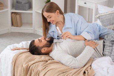 Yatak odasında yatan hamilelik testi olan mutlu genç çift.