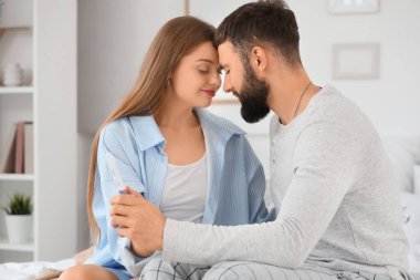 Hamilelik testi olan genç çift yatak odasında el ele tutuşuyor.